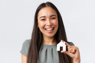 Insurance, loan, real estate and family concept. Close-up of smiling beautiful asian woman buying apartment, found perfect home, showing small paper house and laughing, white background.
